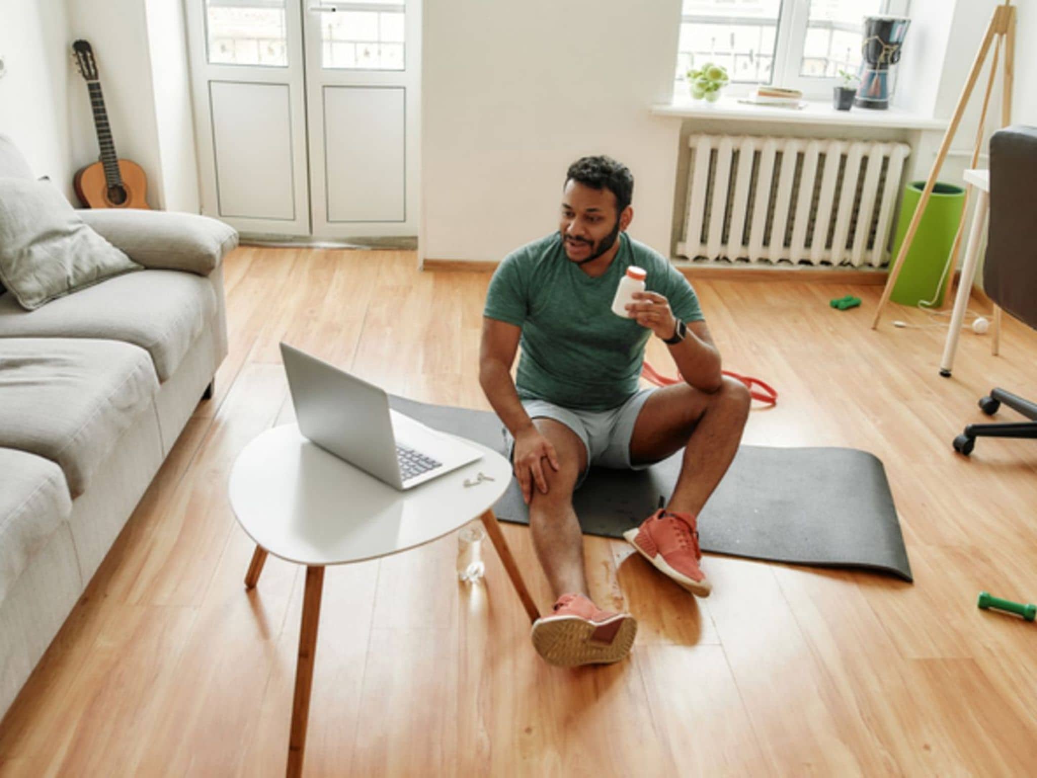 Nahrungsergänzungsmittel beim Sport: Ein Mann sitzt auf einer Gymnastikmatte und trinkt ein Sportgetränk