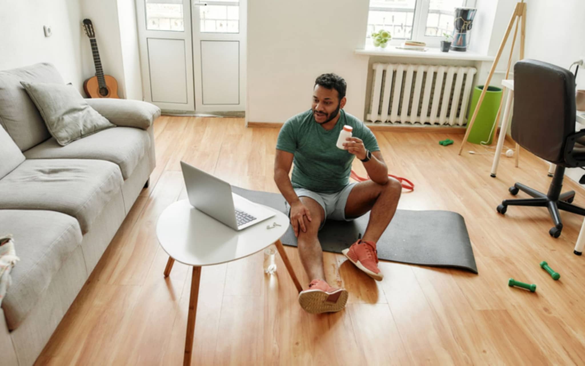 Nahrungsergänzungsmittel beim Sport: Ein Mann sitzt auf einer Gymnastikmatte und trinkt ein Sportgetränk