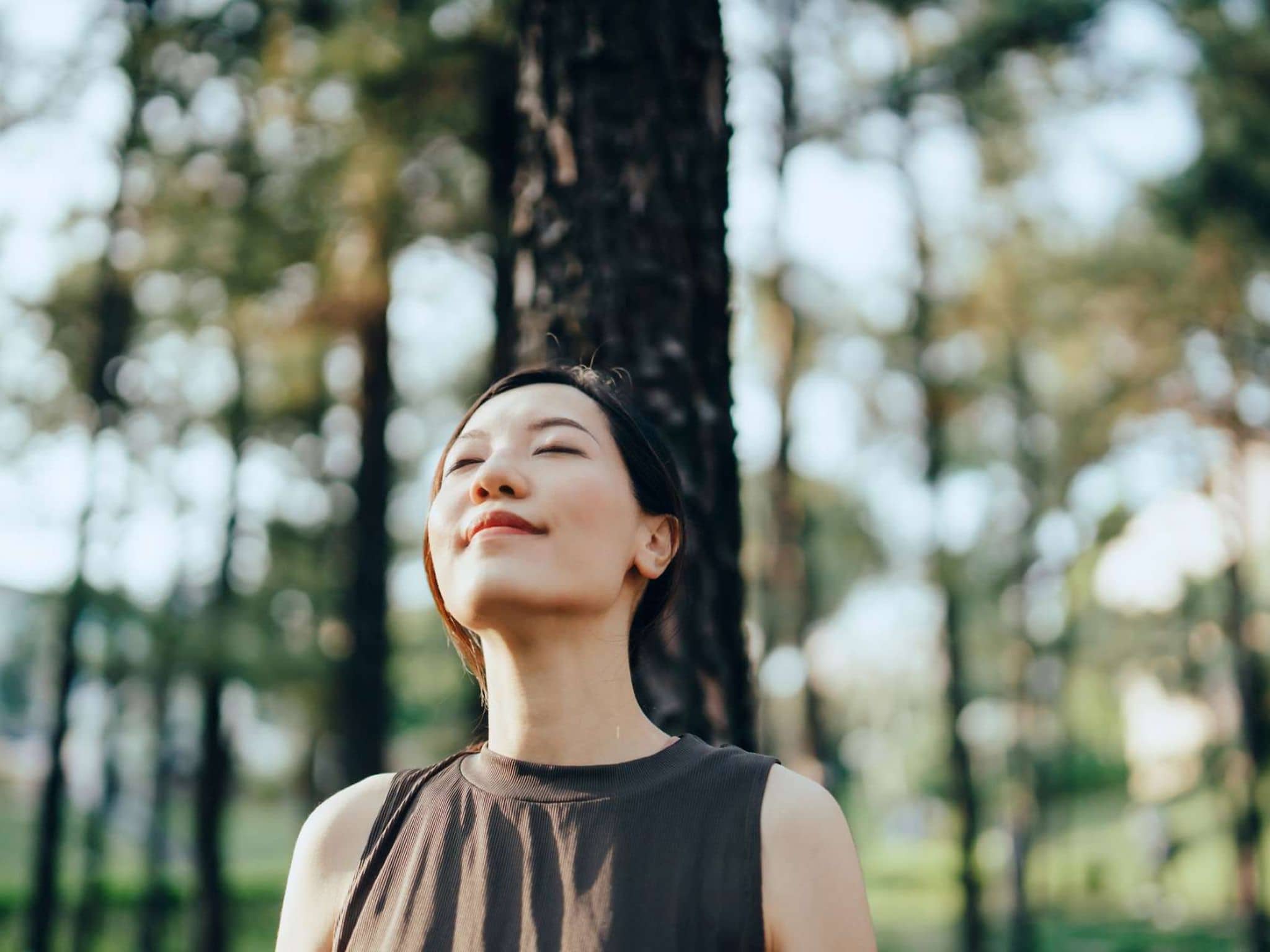 Kraftorte: Junge Frau lehnt sich mit geschlossenen Augen gegen einen Baum im Wald.