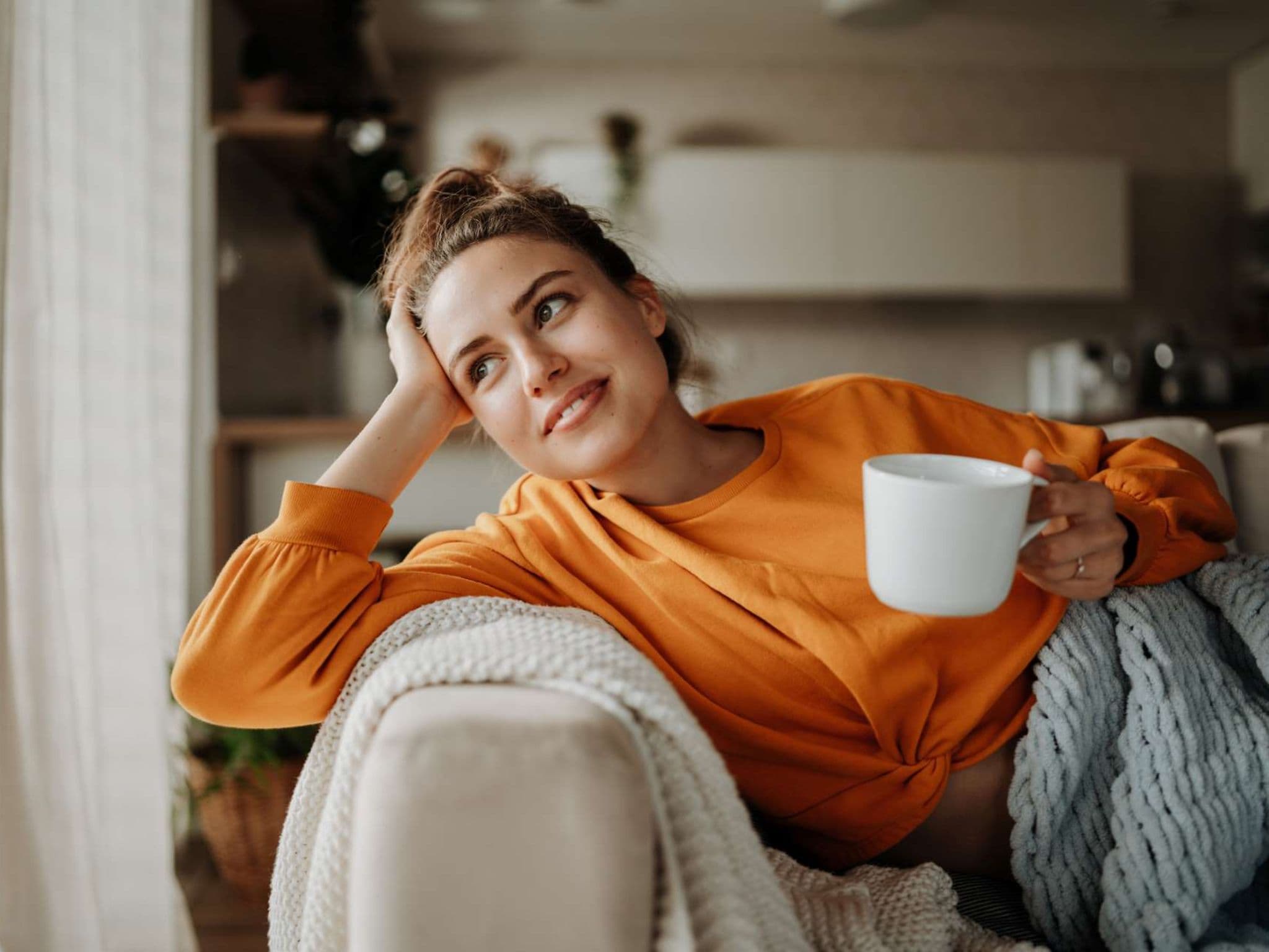 Tipps für Neustart: Eine Frau sitzt gemütlich mit einer Kaffeetasse auf dem Sofa.