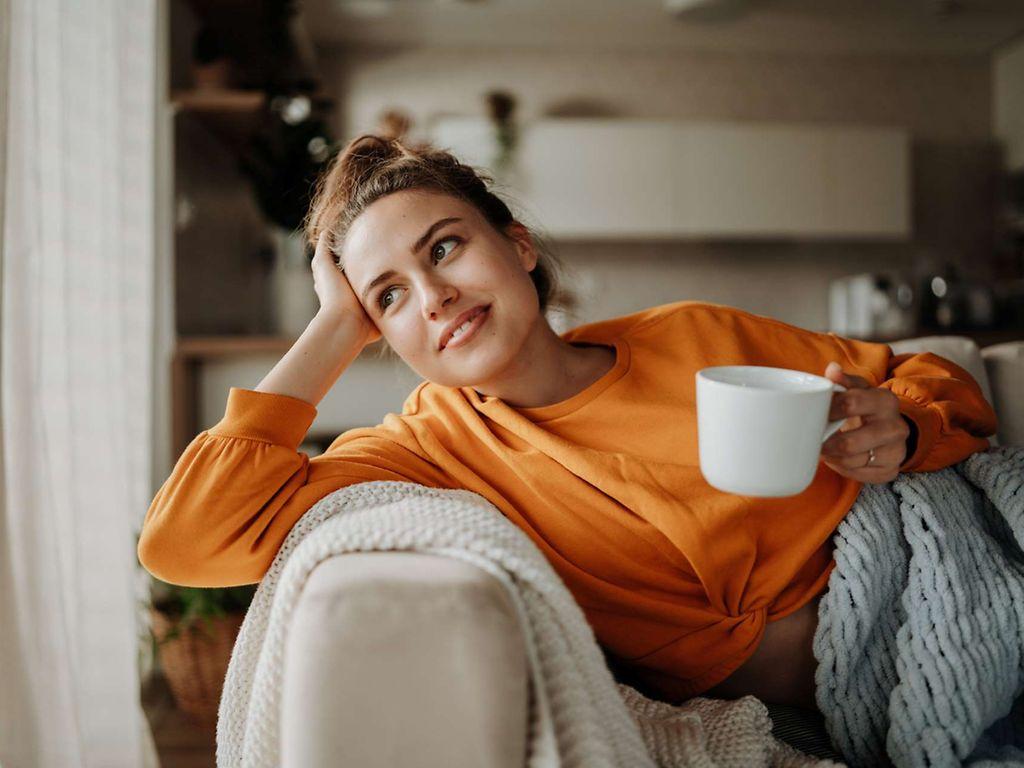 Tipps für Neustart: Eine Frau sitzt gemütlich mit einer Kaffeetasse auf dem Sofa.