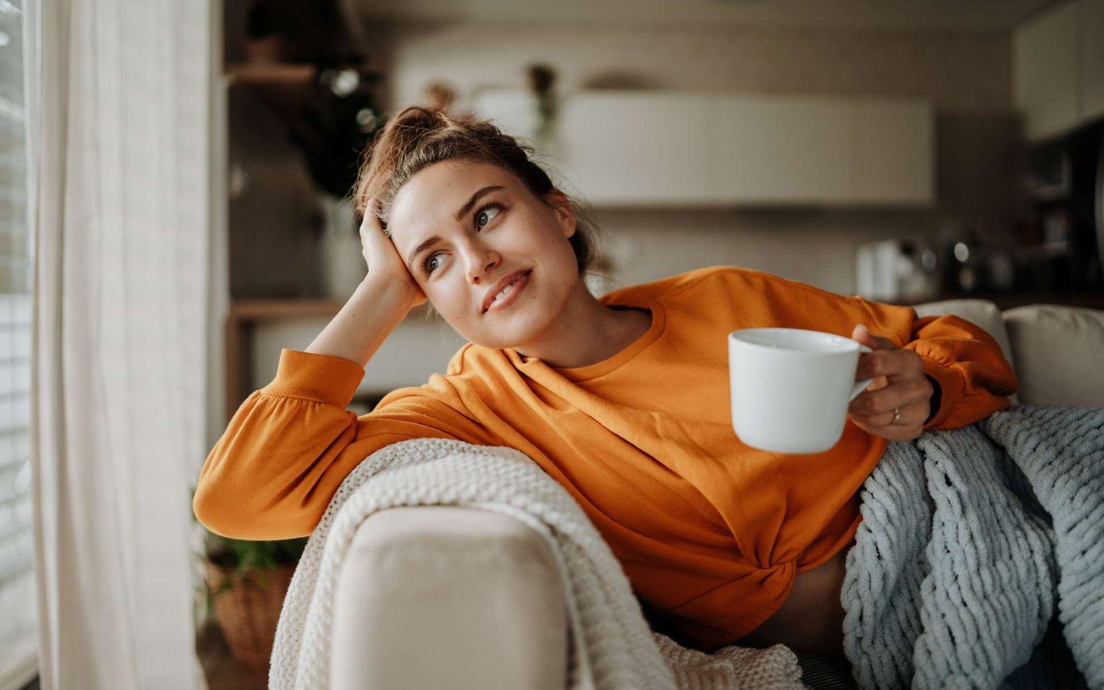 Tipps für Neustart: Eine Frau sitzt gemütlich mit einer Kaffeetasse auf dem Sofa.