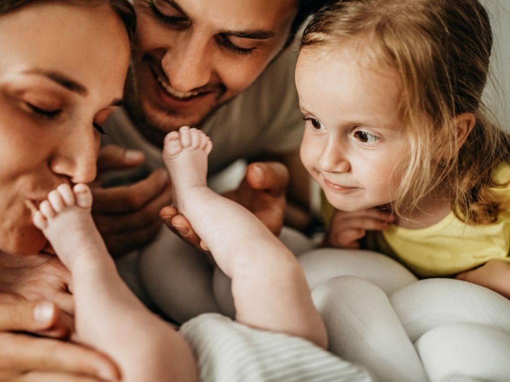Symbolbild für Eifersucht unter Geschwistern: Eltern zeigen ihrem großen Kind das neue Baby