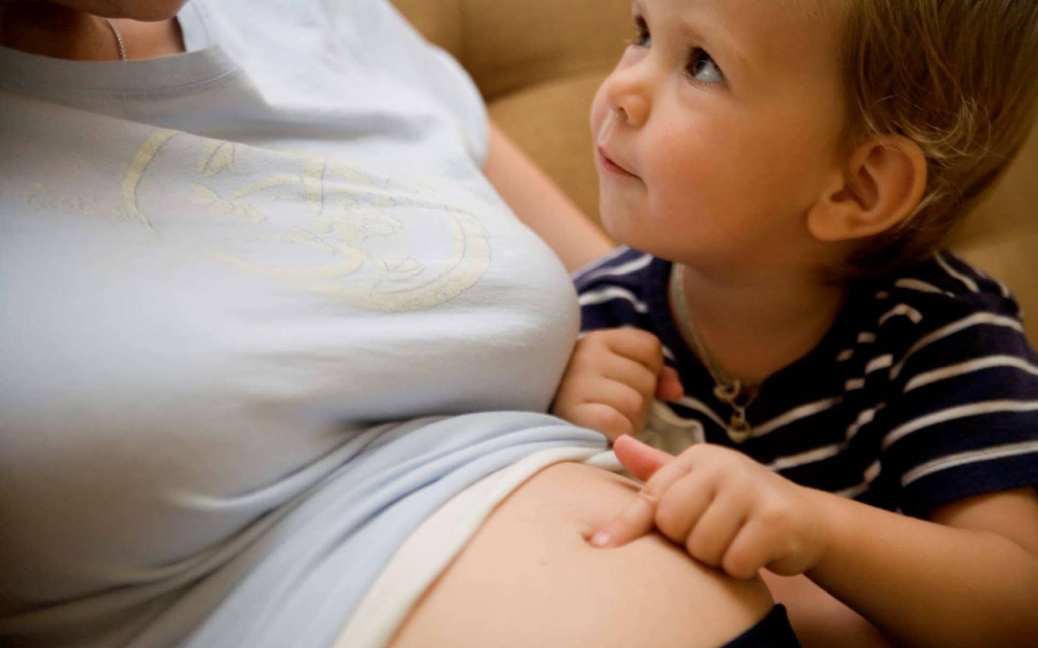Meinen Bauch lieben: Ein Kind tippt mit seinem Finger auf den Bauch seiner Mutter.