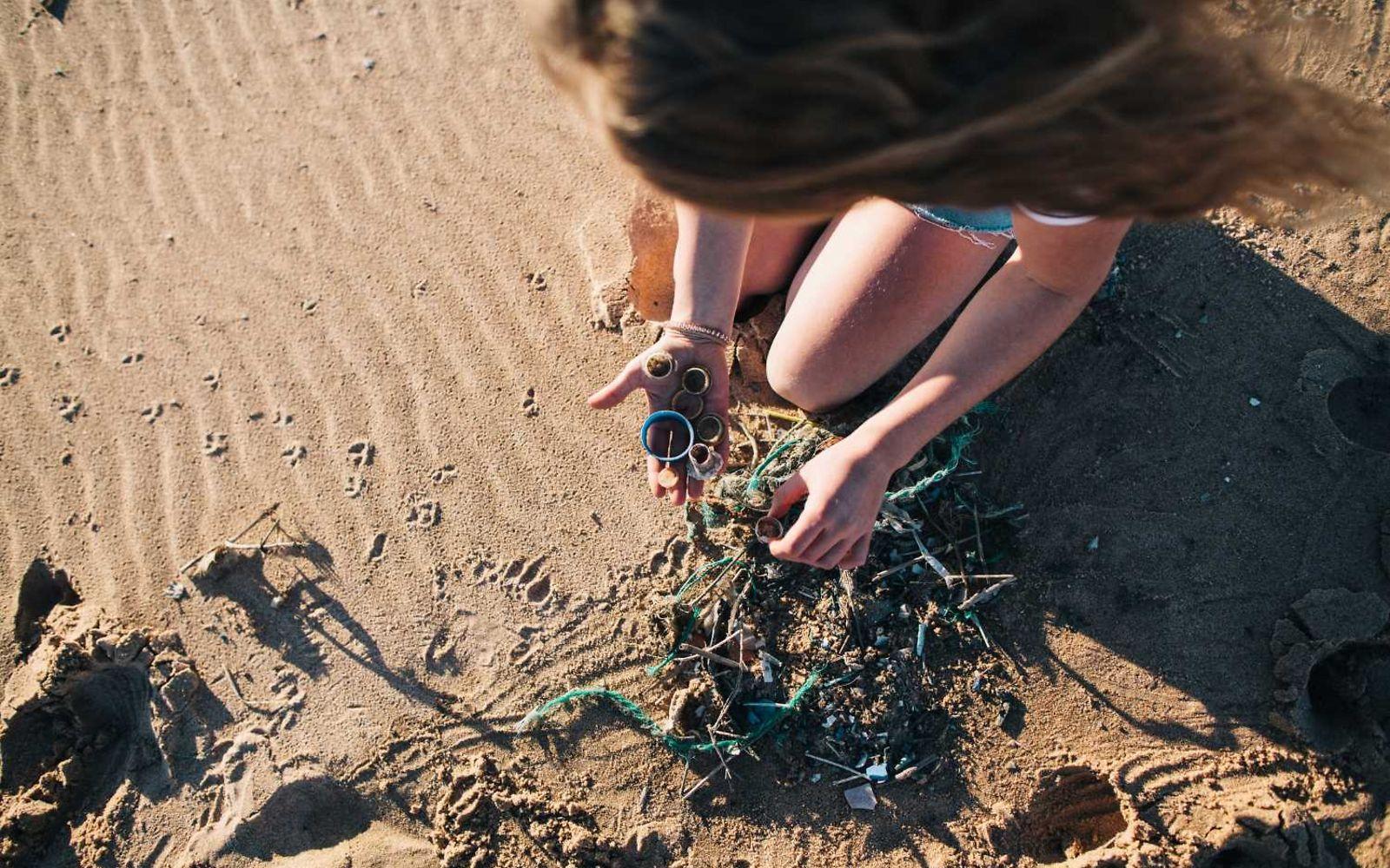 Mikroplastik: Junge Frau sammelt am Strand Kunststoffmüll auf.