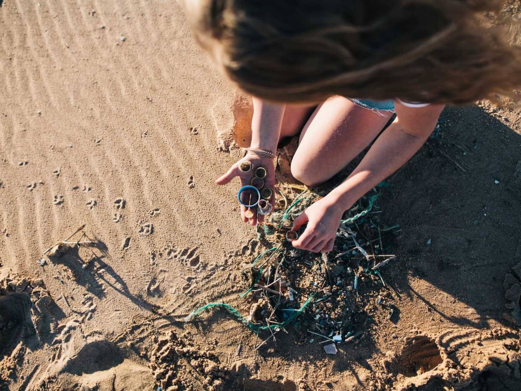Mikroplastik: Junge Frau sammelt am Strand Kunststoffmüll auf.