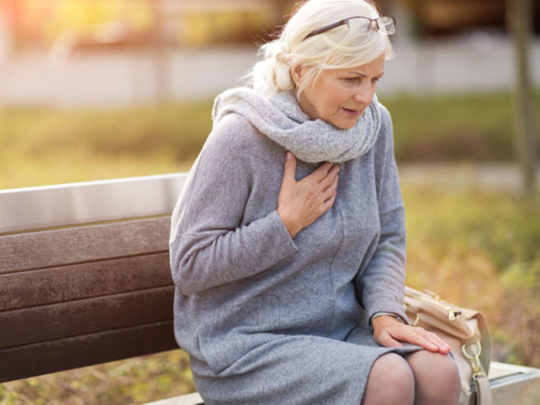Lungenembolie: Ältere Dame sitzt auf einer Parkbank und ringt nach Luft