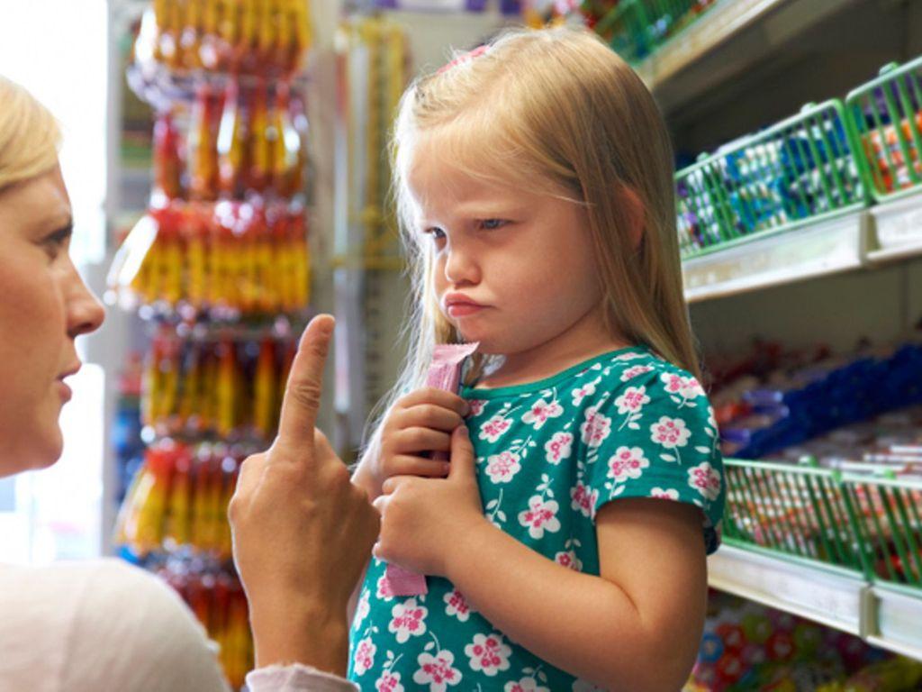 Wut in der Erziehung: Eine Mutter schimpft mit ihrer kleinen Tochter vor dem Süßigkeitenregal eines Supermarkts