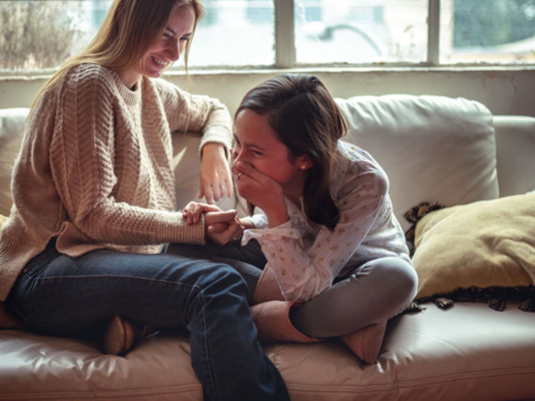 Mutter und Tochter sitzen vertraut auf der Couch und die Tochter lacht mit der Hand vor dem Mund