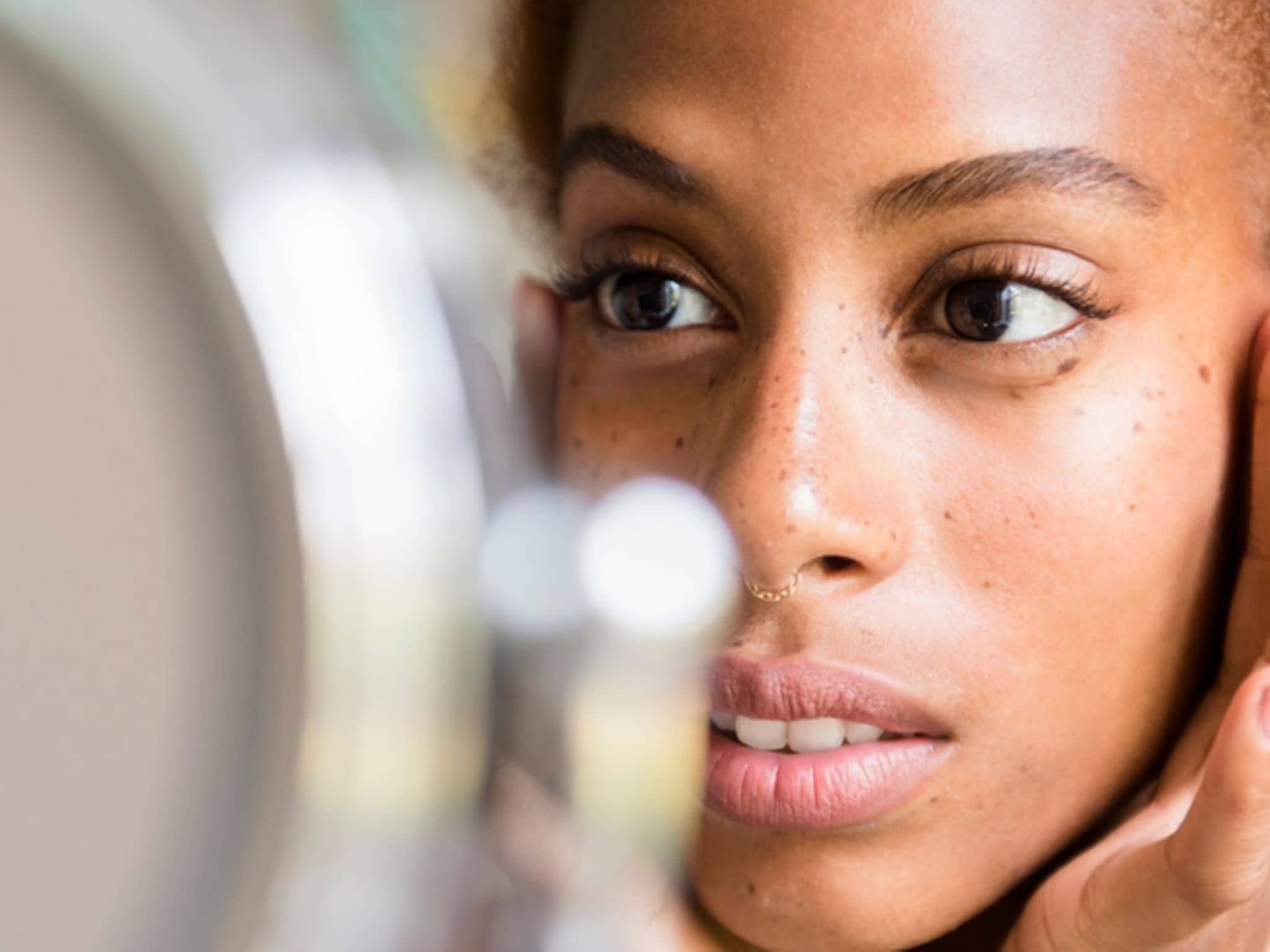 Pigmentstörungen: Junge Frau betrachtet im Spiegel ihr Gesicht