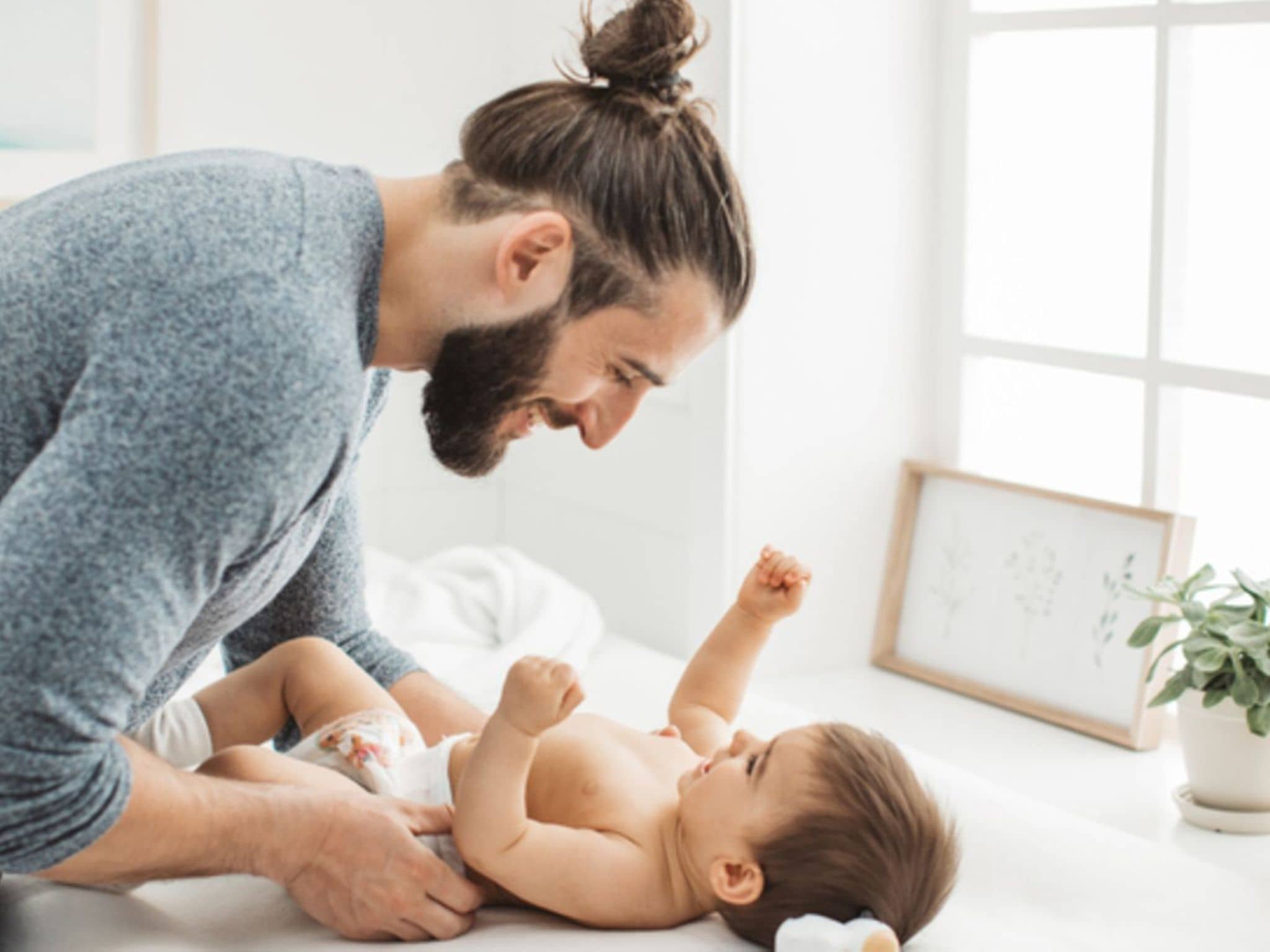 Junger Vater, der mit seinem kleinen Mädchen spielt, während er die Windel auf dem Wickeltisch umzieht