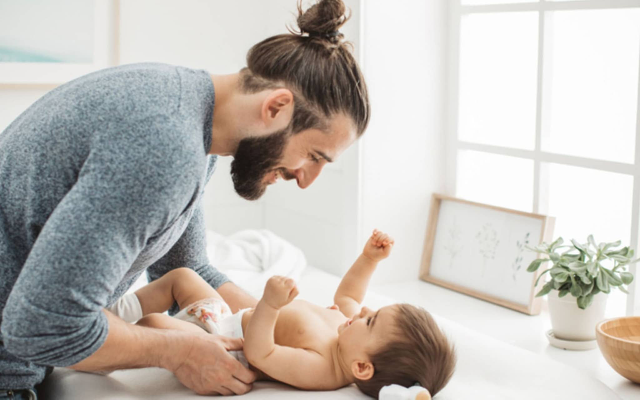 Junger Vater, der mit seinem kleinen Mädchen spielt, während er die Windel auf dem Wickeltisch umzieht