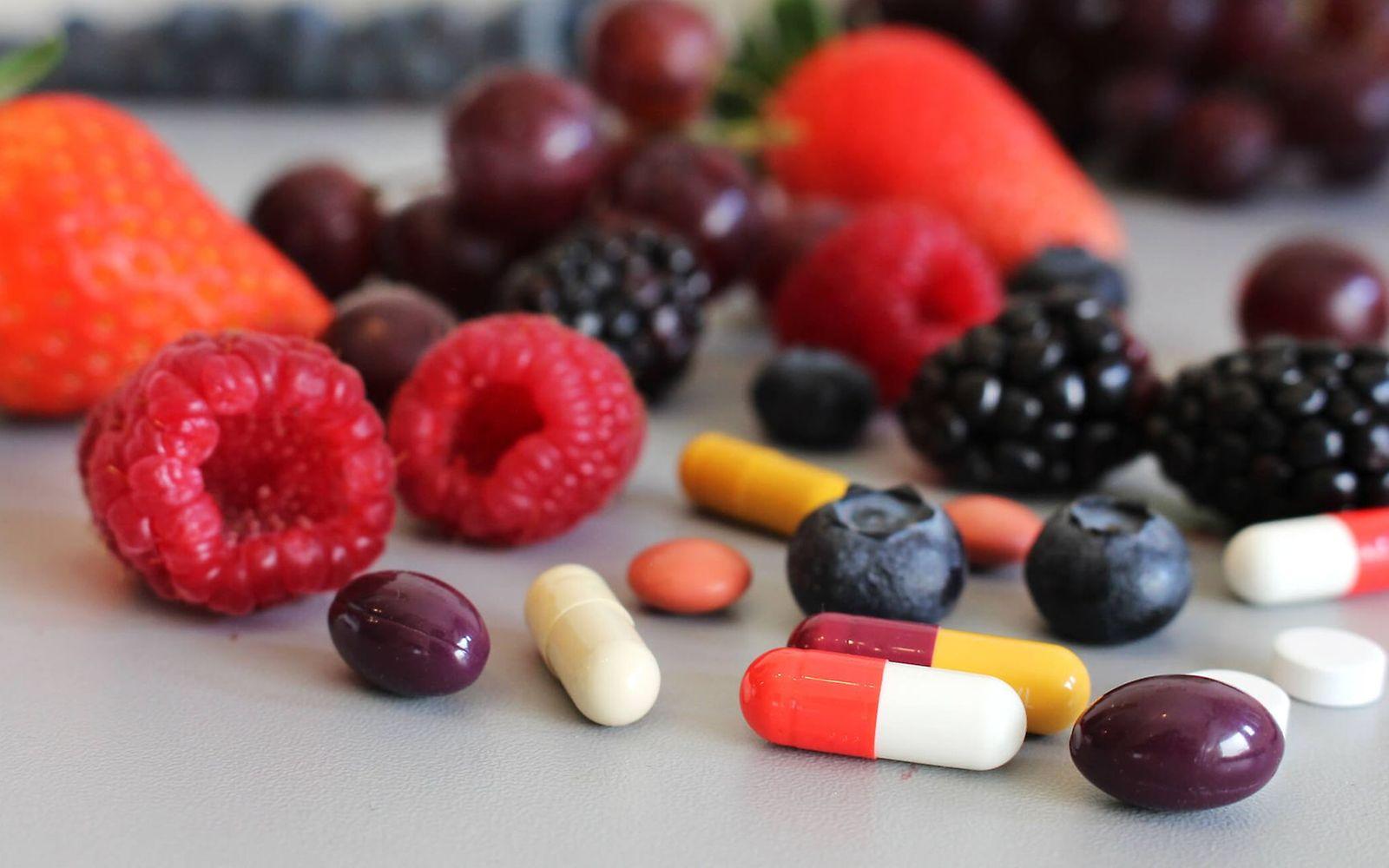 Nahrungsergänzungsmittel: Auf einem Tisch liegen Pillen und Obst.