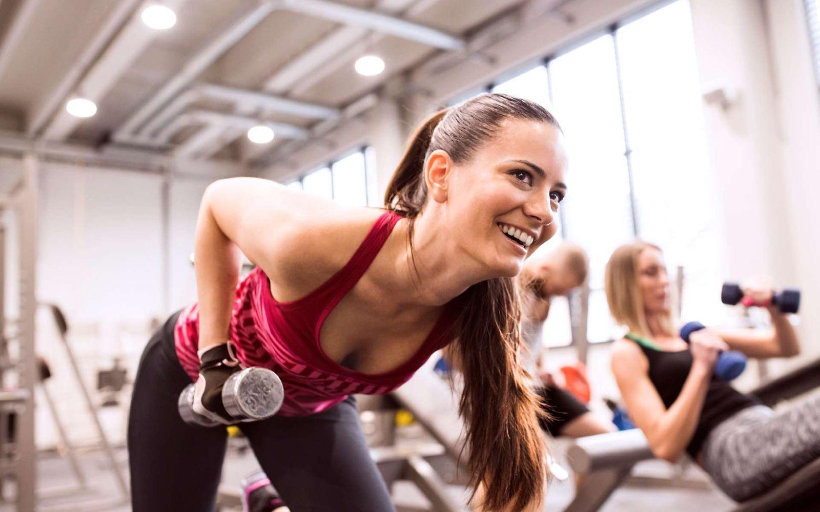 Freude beim Krafttraining: Eine junge Frau trainiert in einem Fitnessstudio mit Hanteln.