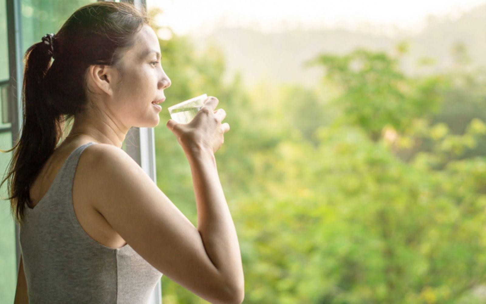 Reger Stoffwechsel: Frau trinkt ein Glas Wasser und schaut aus dem Fenster
