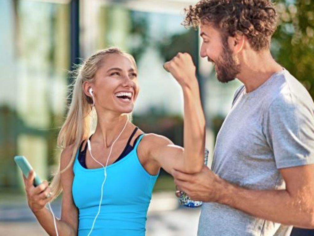 Sportmotivation: Junge Frau flext ihre Armmuskeln vor ihrem Freund
