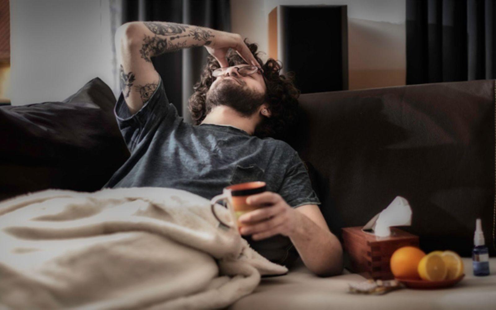 Fatigue Syndrom: Mann liegt erschöpft auf der Couch und fasst sich an die Stirn