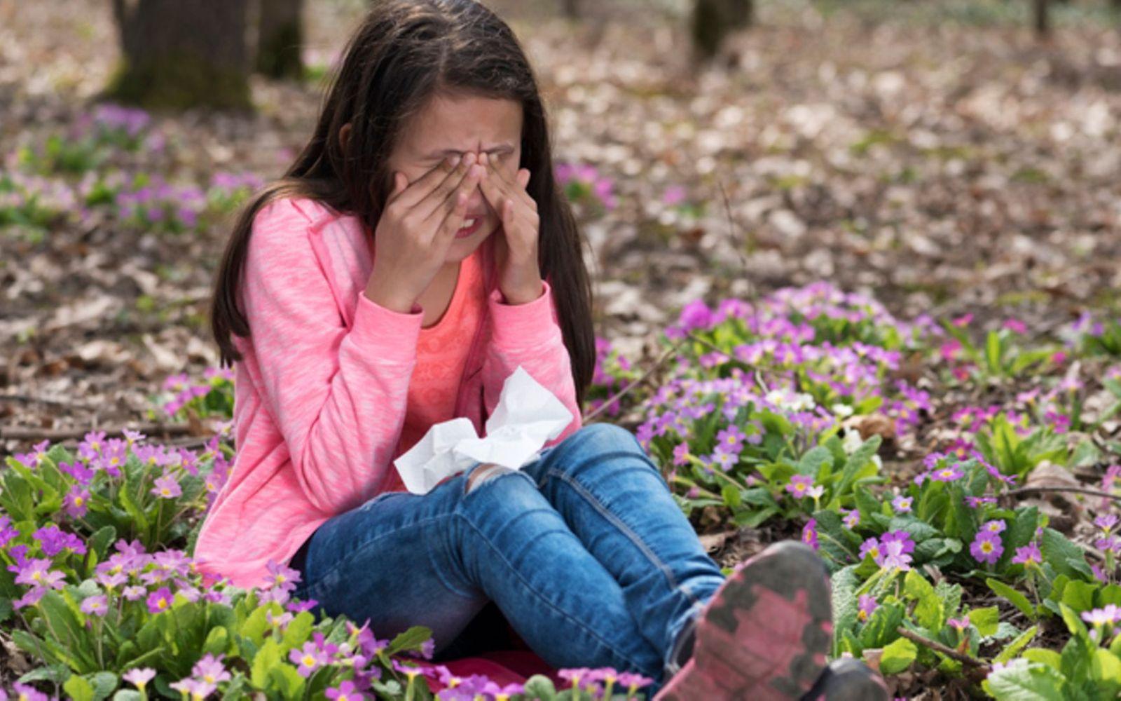 Symbolbild für Heuschnupfen bei Kindern: Ein kleines Mädchen sitzt auf einer Blumenwiese und reibt sich die Augen