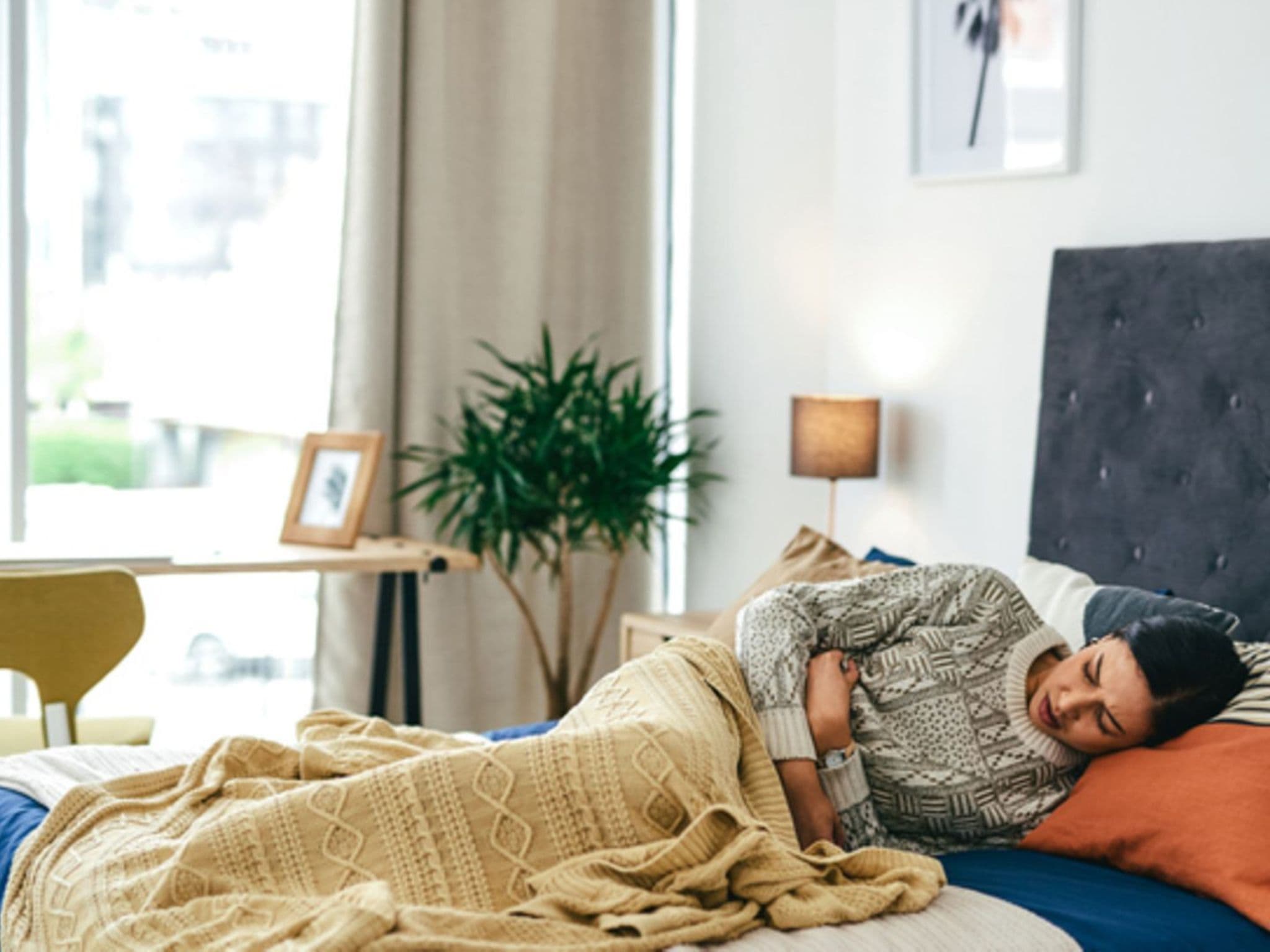 Endometriose: Eine Frau liegt auf einem Bett und hält sich ihren Bauch