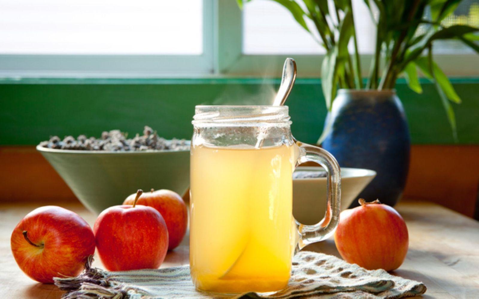 Apfelessig: Auf einem Tisch steht ein Glas Apfelessig. Daneben liegen einige Äpfel.