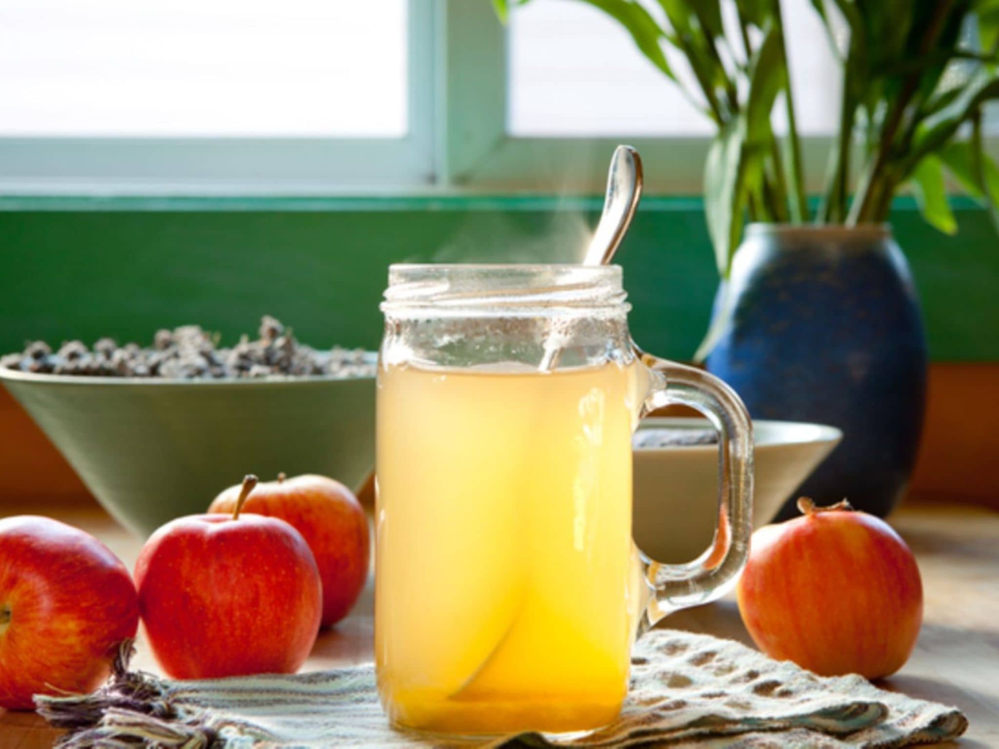 Apfelessig: Auf einem Tisch steht ein Glas Apfelessig. Daneben liegen einige Äpfel.