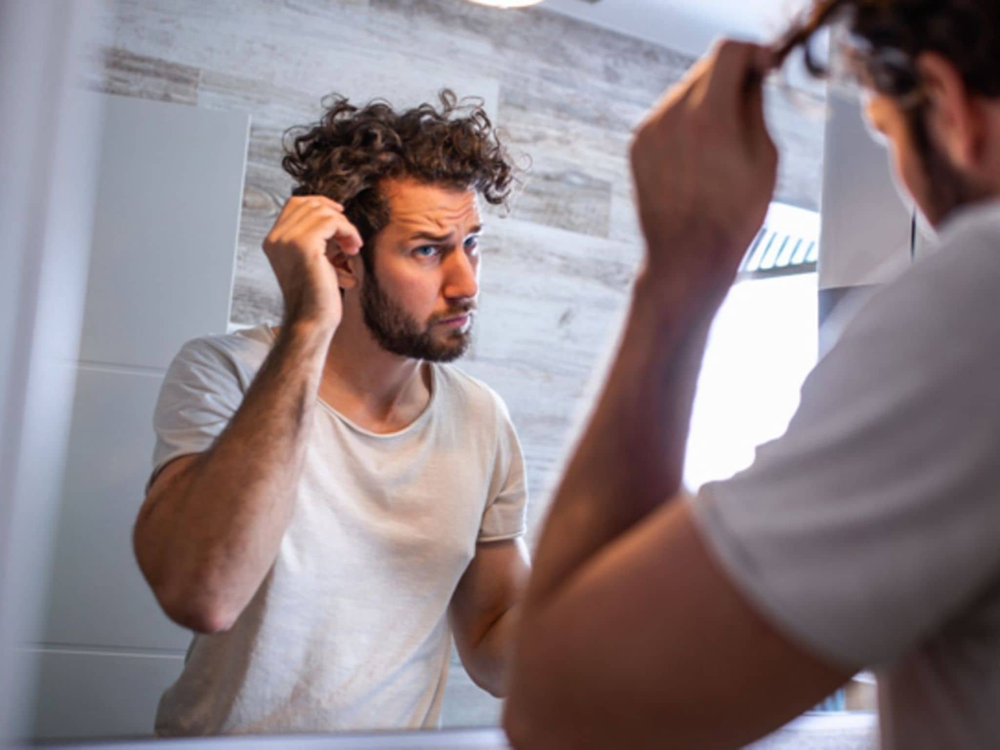 Haarausfall: Mann guckt skeptisch in den Spiegel und fasst sich ins Haar