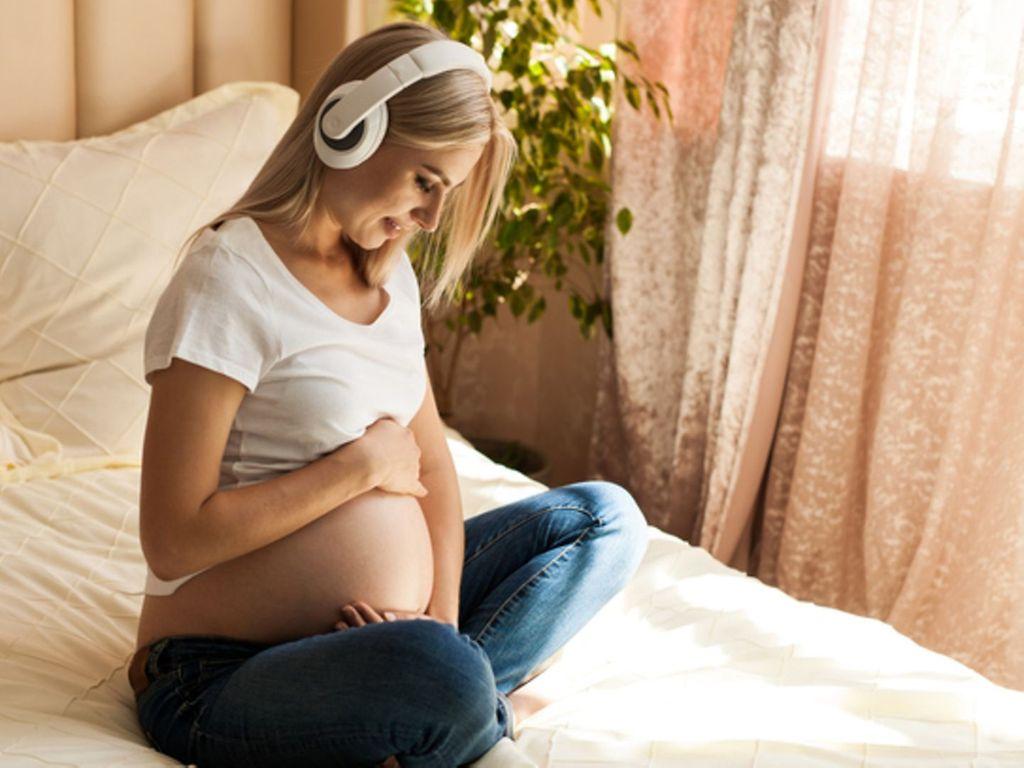 Meditation in der Schwangerschaft: Eine schwangere Frau meditiert auf dem Bett sitzend