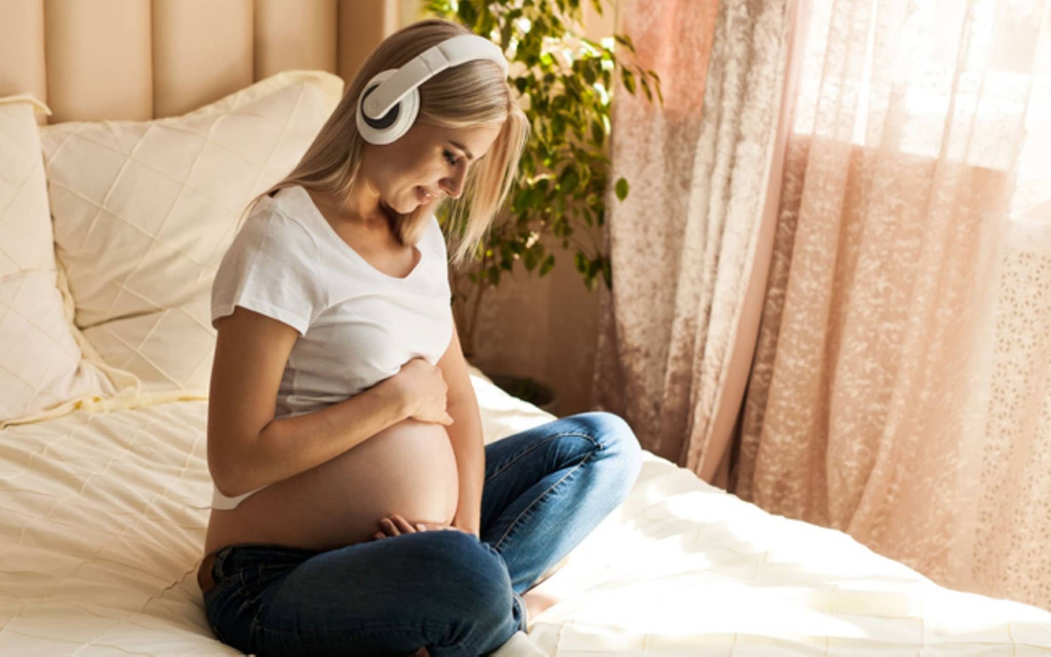 Meditation in der Schwangerschaft: Eine schwangere Frau meditiert auf dem Bett sitzend