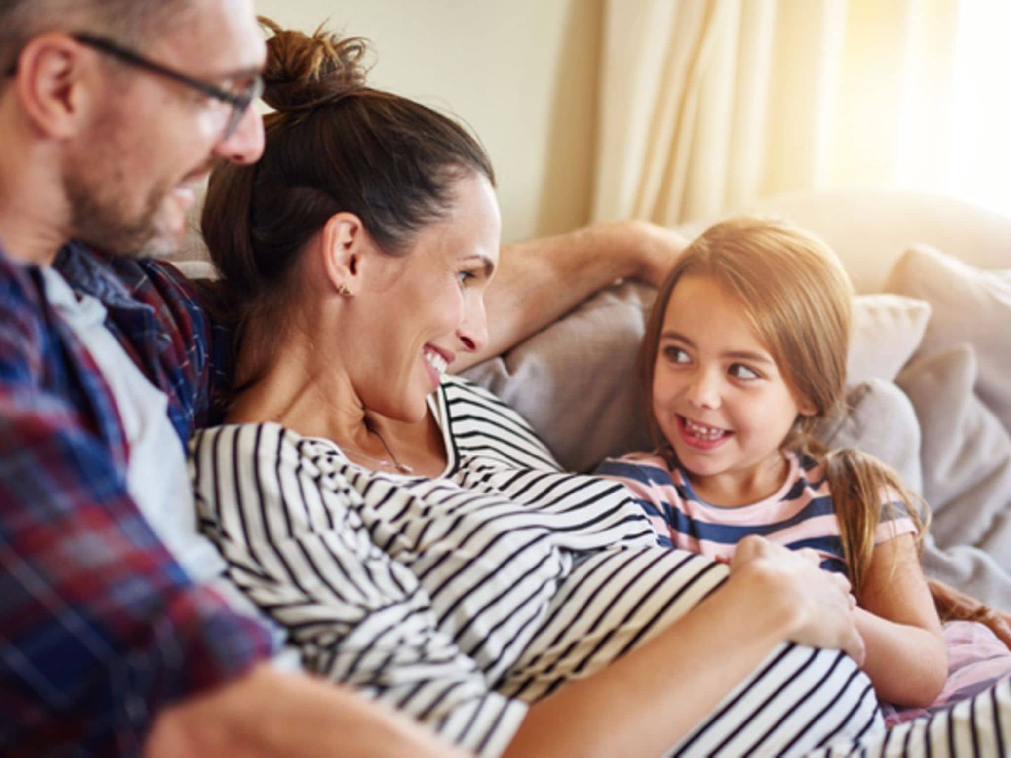 Zweite Schwangerschaft: Schwangere Frau sitzt mit Mann und kleiner Tochter auf dem Sofa