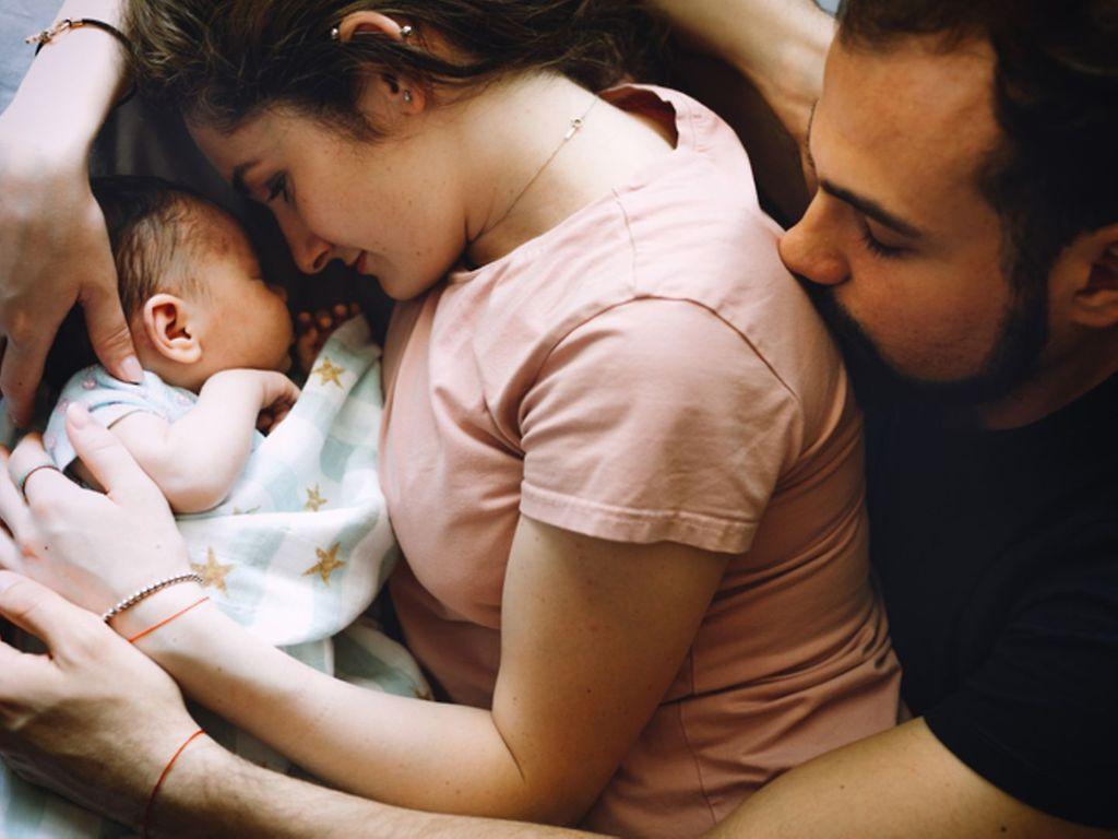 Wochenbett: Paar liegt mit neugeborenem Säugling im Bett