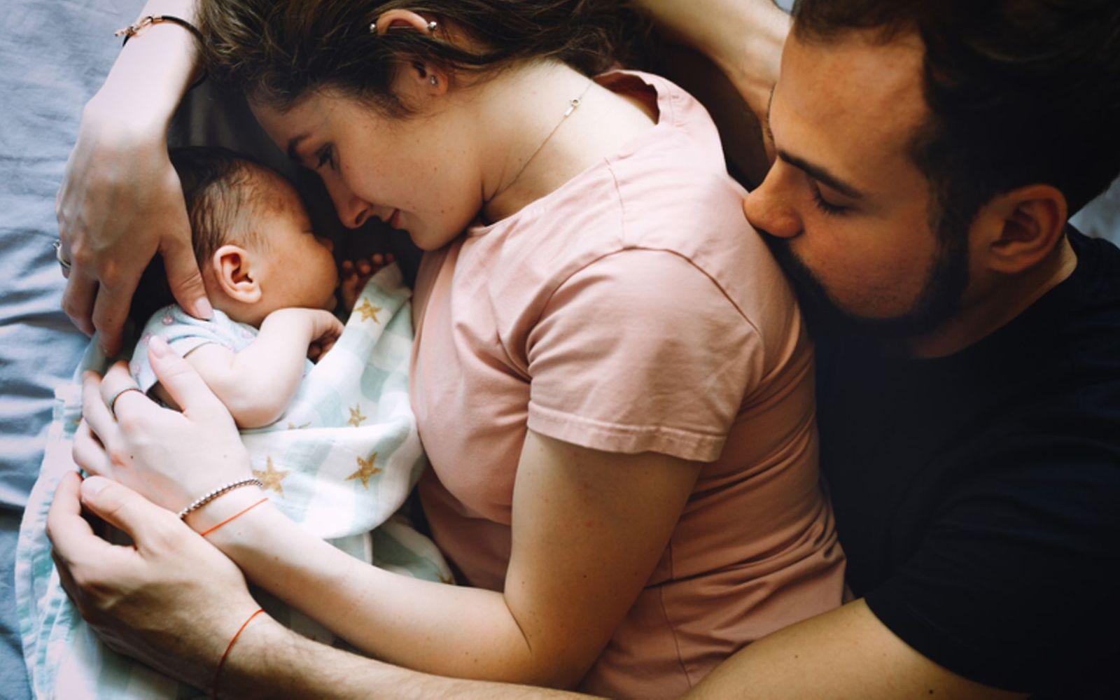 Wochenbett: Paar liegt mit neugeborenem Säugling im Bett