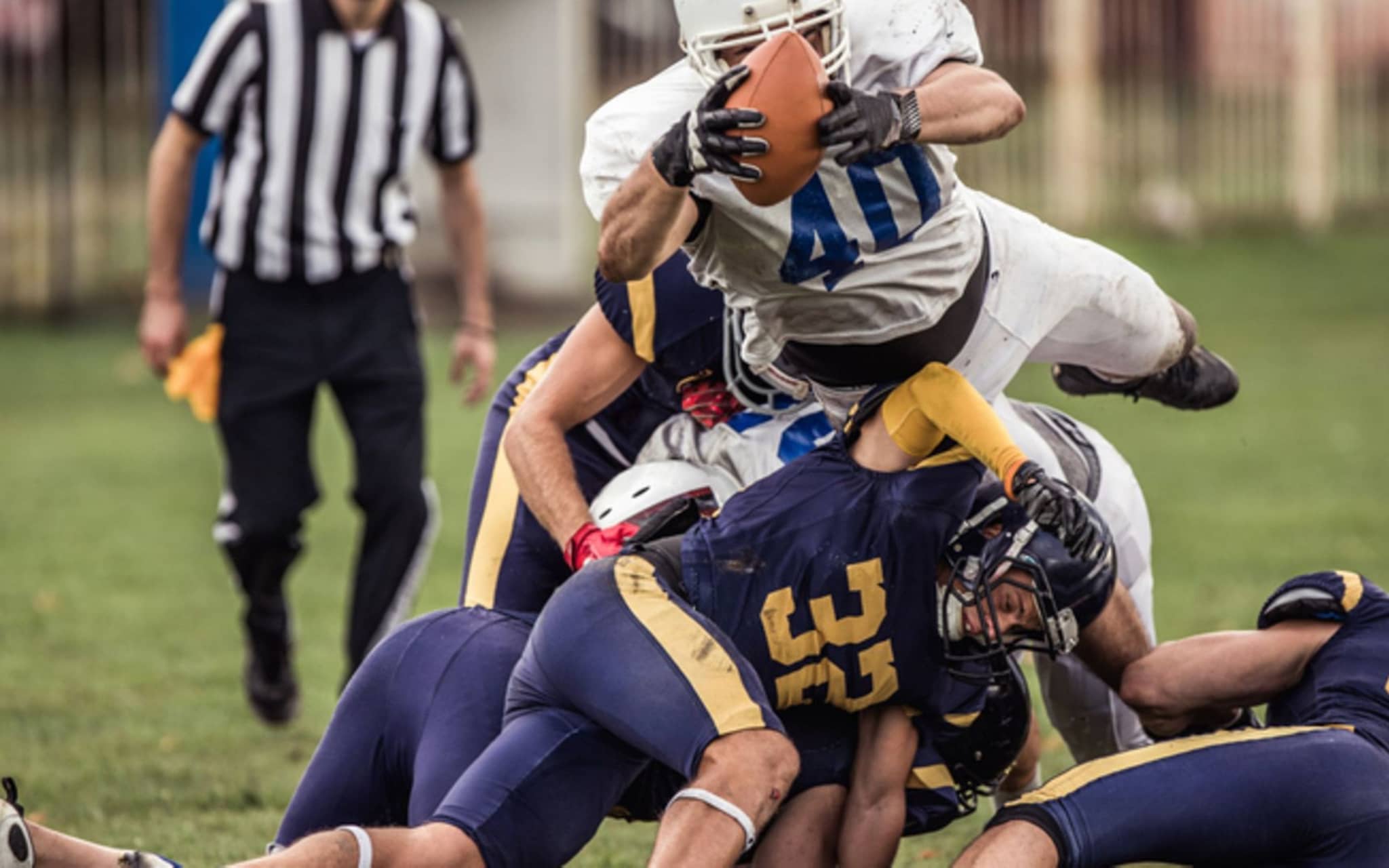 American Football: Mehrere Football-Spieler in voller Montur fallen bei einem Spiel übereinander her.