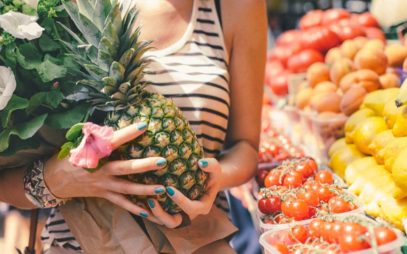 Vegane Ernährung: Frau hat auf einem Wochenmarkt eine Ananas gekauft.