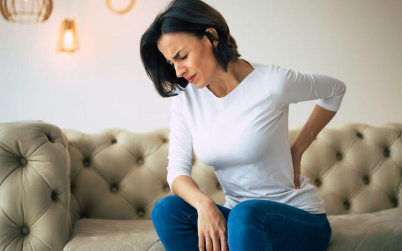 Nierenerkrankung: Frau fasst sich mit schmerzverzerrtem Gesicht an den unteren Rücken