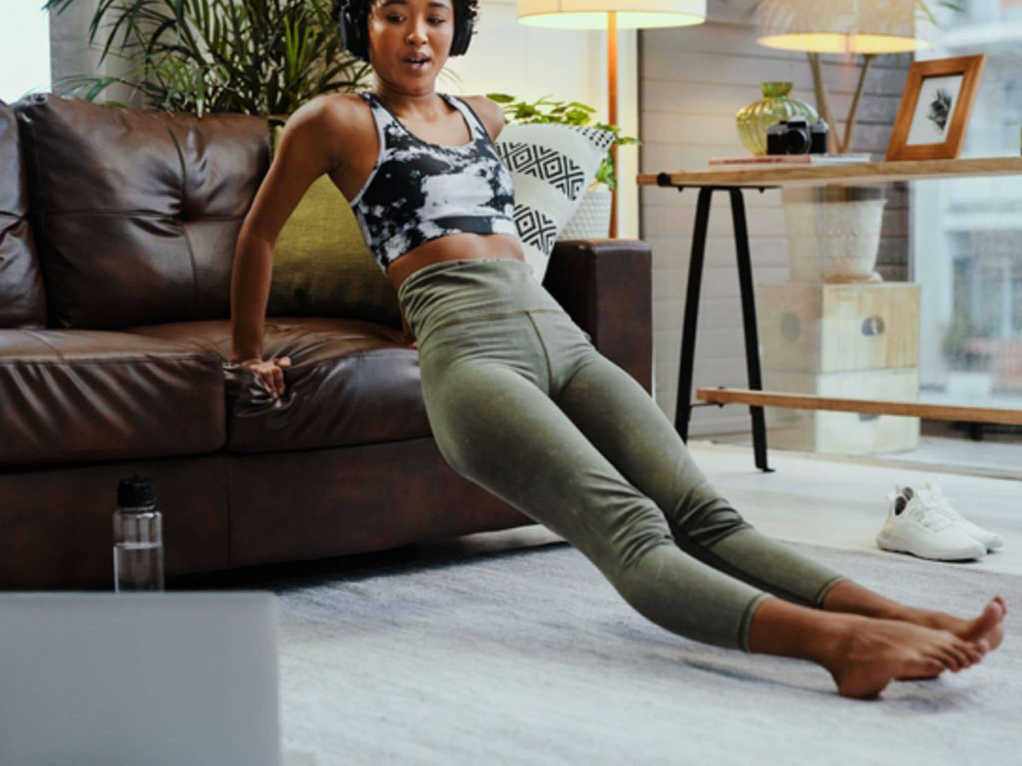 Virtuelle Trainingspartner: Junge Frau macht Sport in Ihrem Wohnzimmer und schaut dabei auf ihr Notebook.