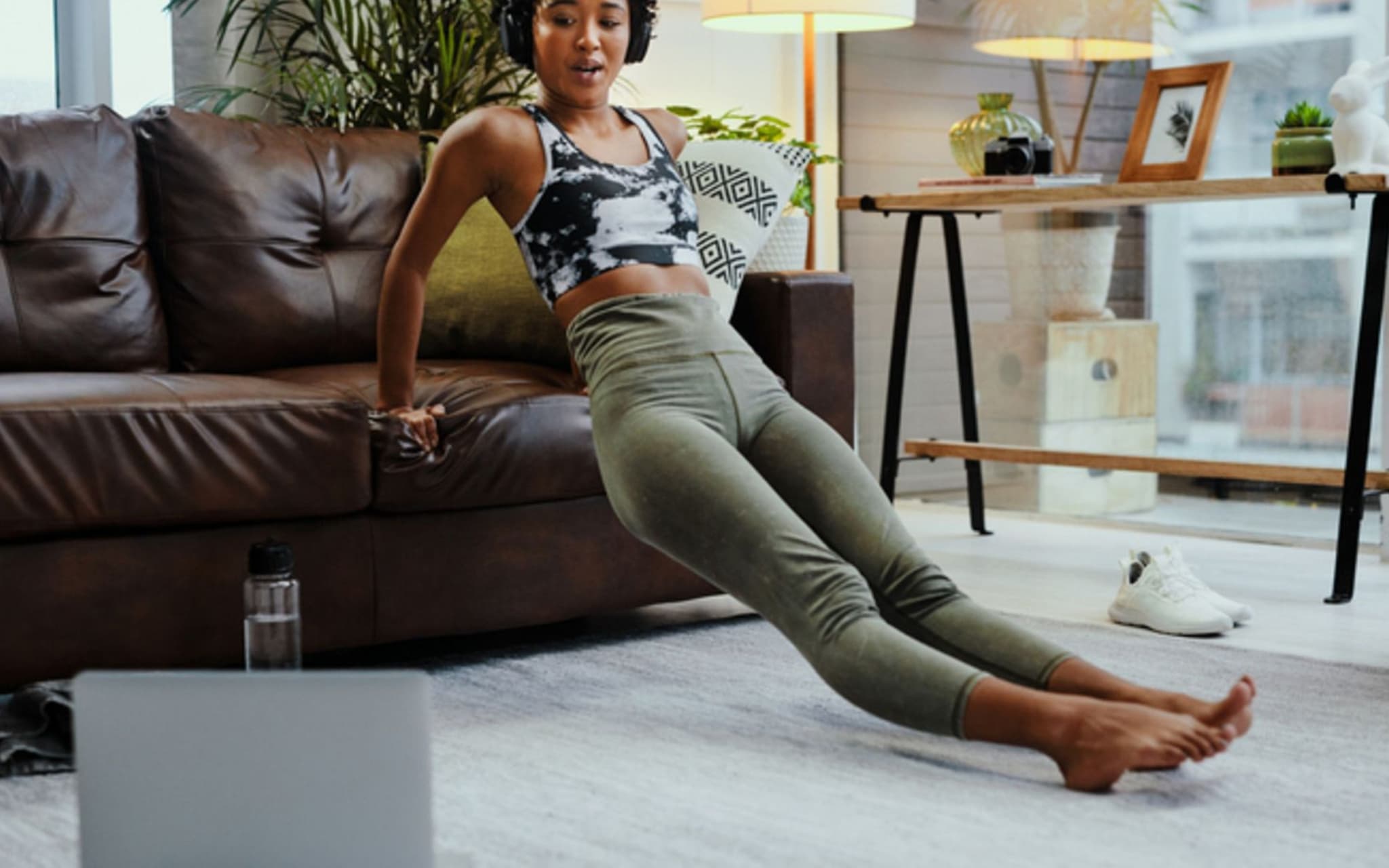 Virtuelle Trainingspartner: Junge Frau macht Sport in Ihrem Wohnzimmer und schaut dabei auf ihr Notebook.