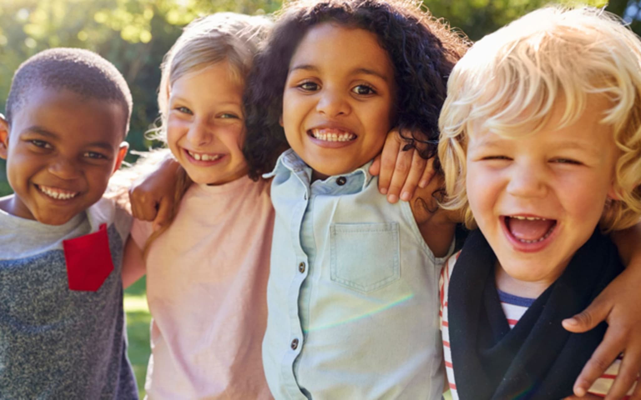 Tics bei Kindern: Vier kleine Kinder legen die Arme umeinander und lachen in die Kamera
