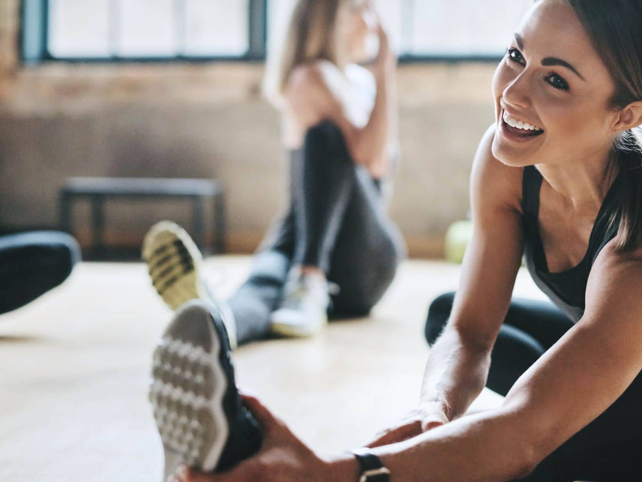 Zähne und Fitness: Lächelnde Frau dehnt sich gemeinsam mit anderen Teilnehmerinnen eines Fitnesskurses.
