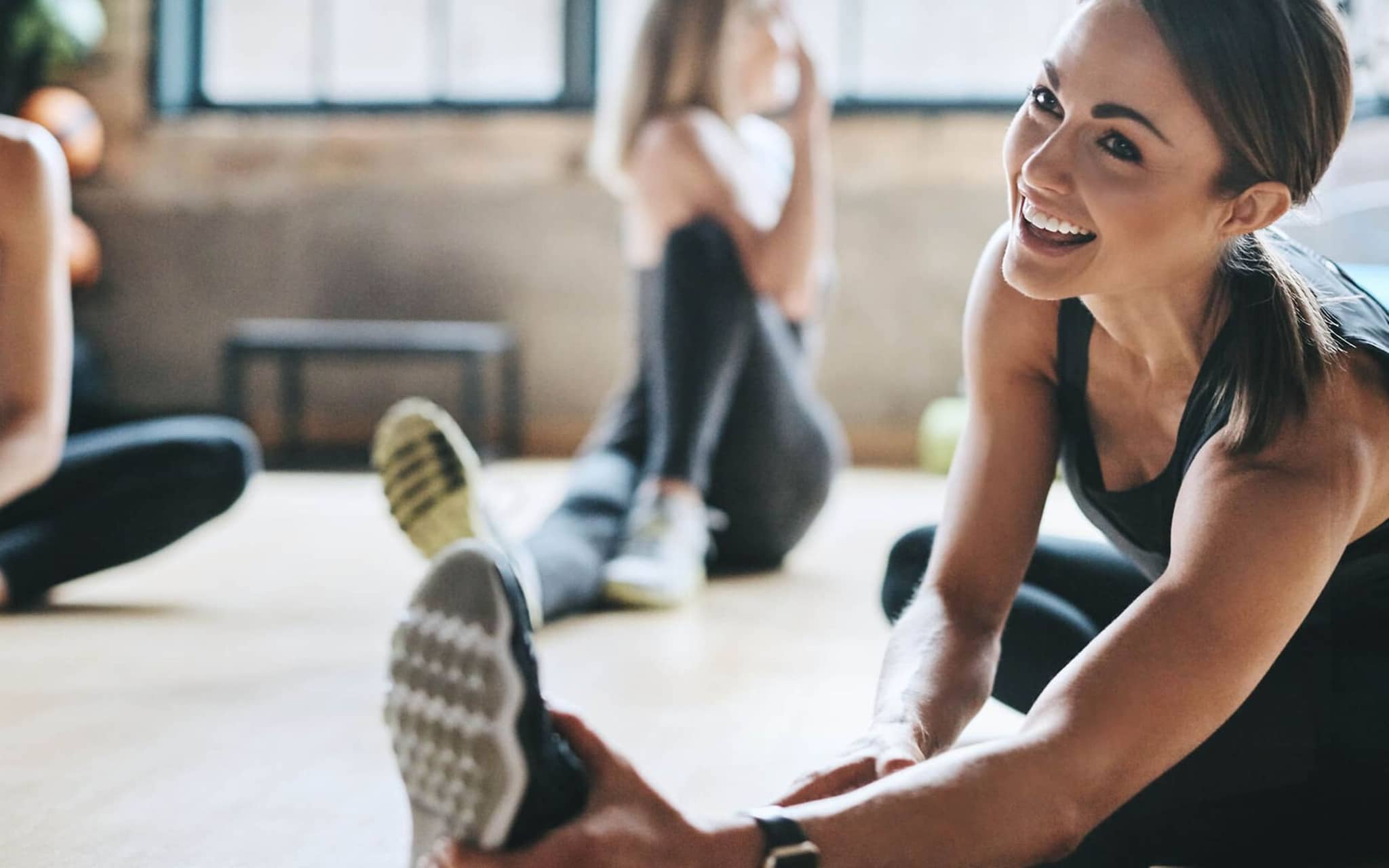 Zähne und Fitness: Lächelnde Frau dehnt sich gemeinsam mit anderen Teilnehmerinnen eines Fitnesskurses.