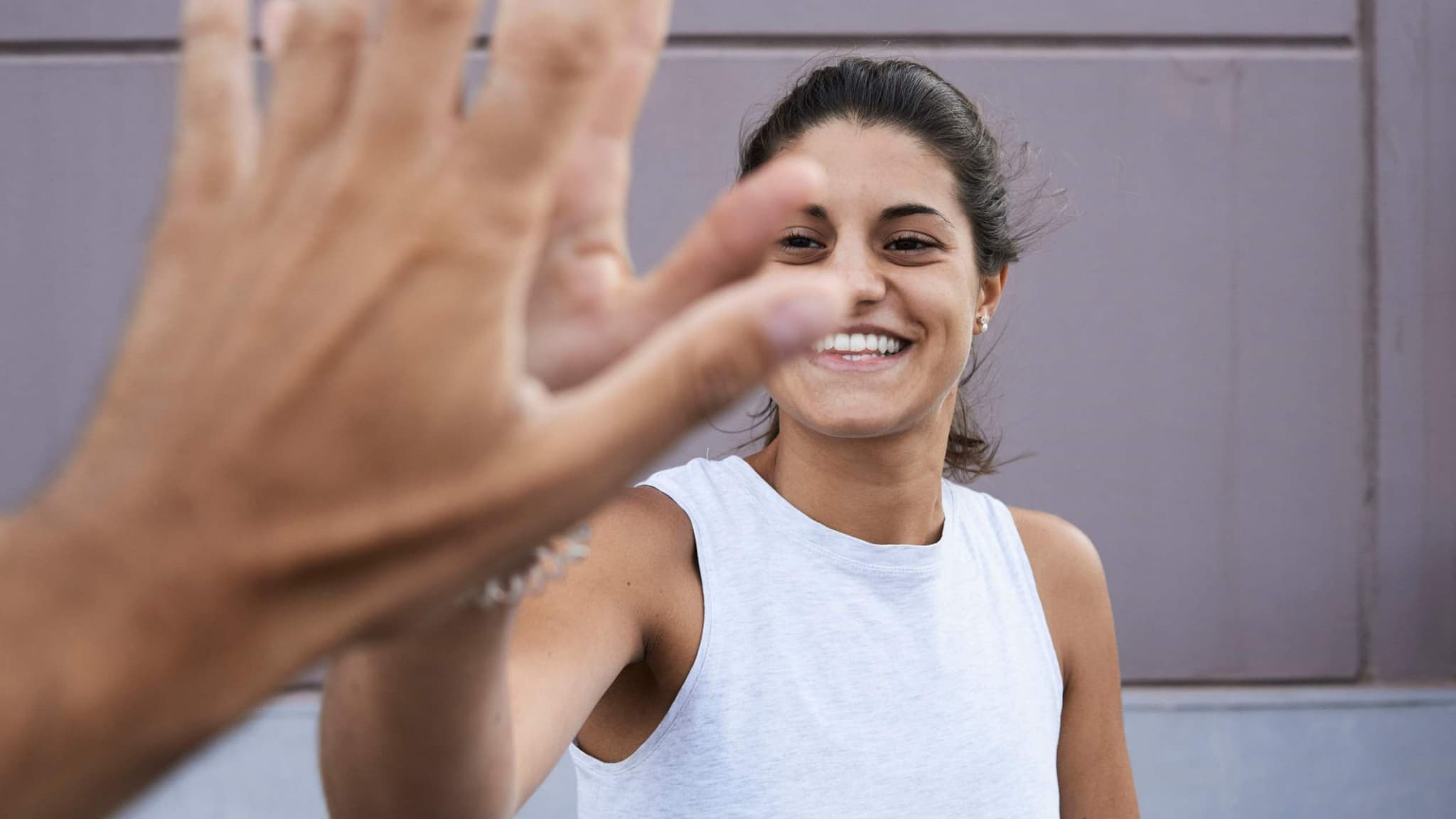 Frauengesundheit: Lächelnde Frau im sportlichen weißen T-Shirt klatscht sich ab im Spiegelbild.