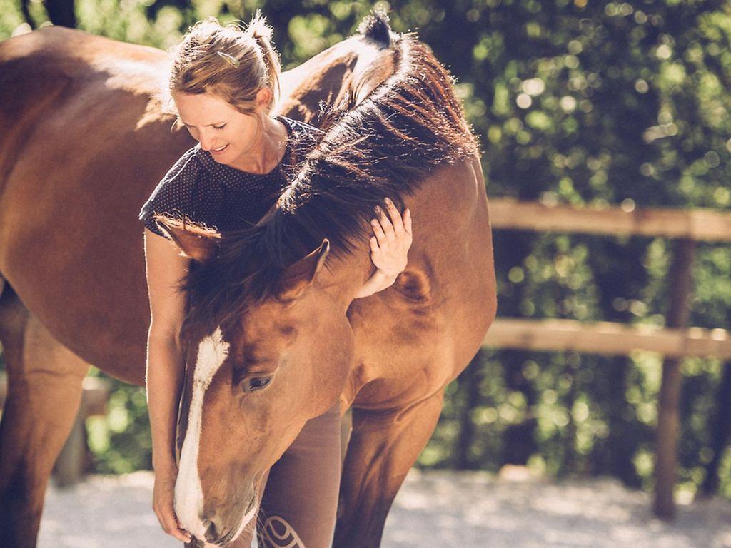 Reiten für die Gesundheit: Eine Frau streichelt ihr Pferd.