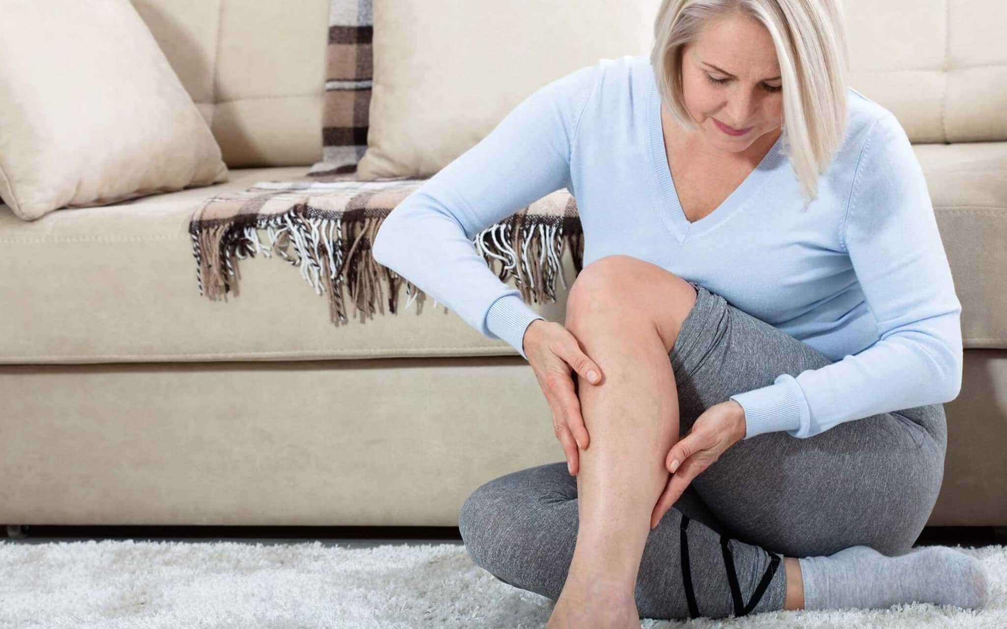 Thrombose: Eine Frau fasst sich an ihre Wade