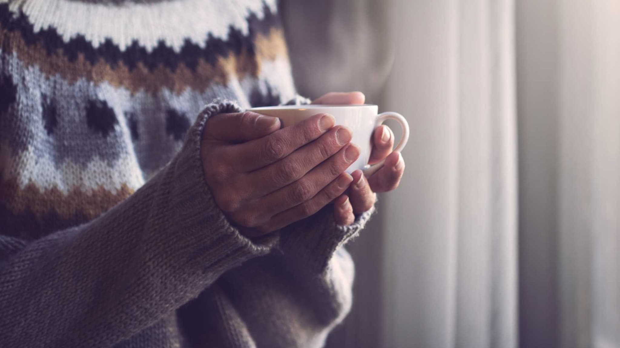 Grippe: Hände umschließen Tasse, aus der Dampf aussteigt.