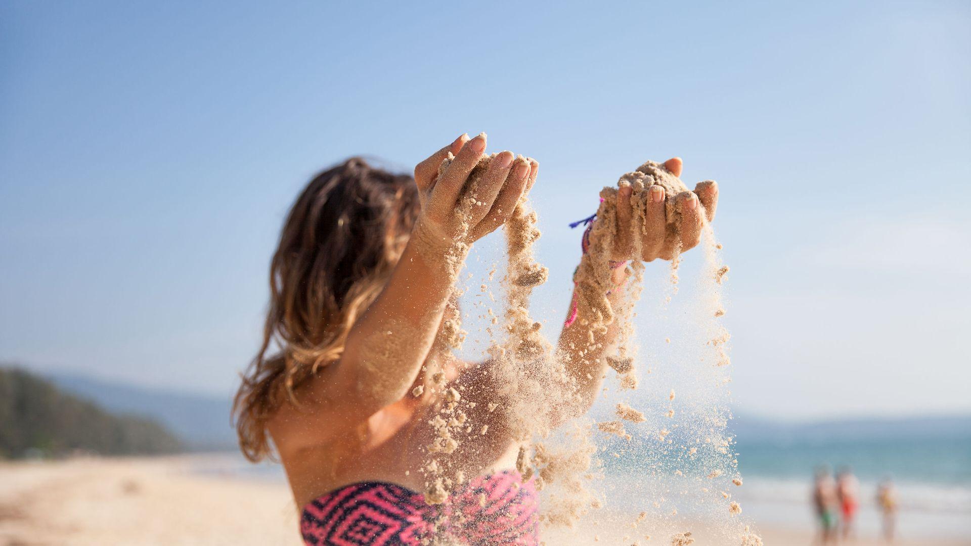 Sonne und Haut: Kind am Strand lässt Sand durch die Hände rieseln.