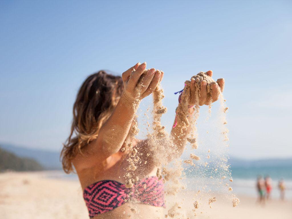 Sonne und Haut: Kind am Strand lässt Sand durch die Hände rieseln.