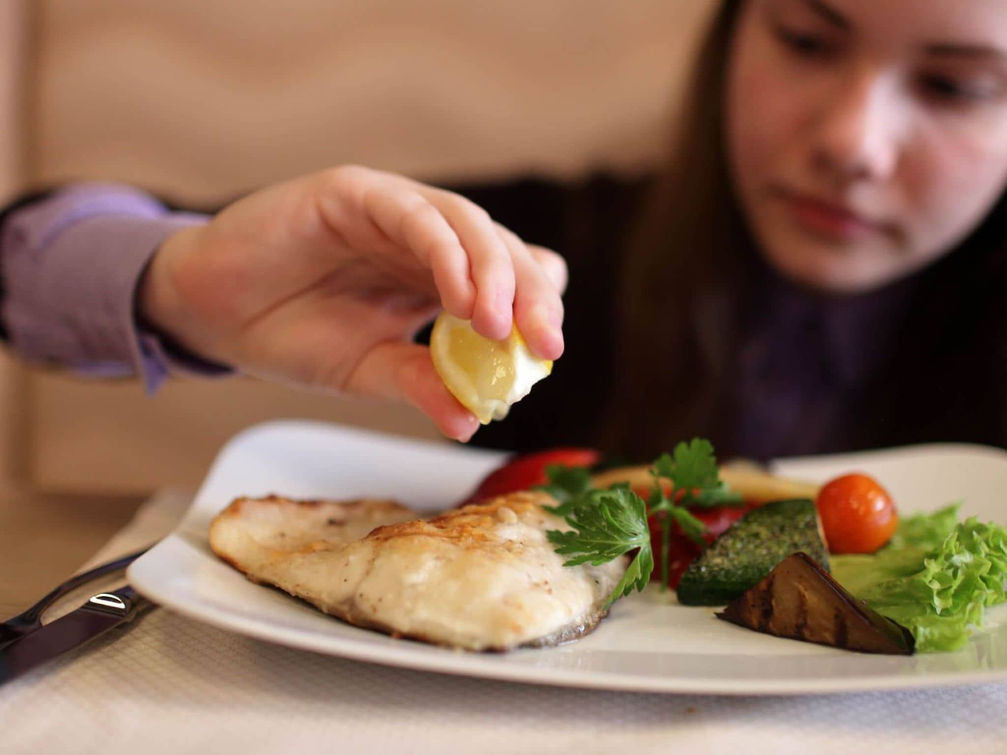 Junges Mädchen macht Zitrone auf ihren Fisch auf dem Teller