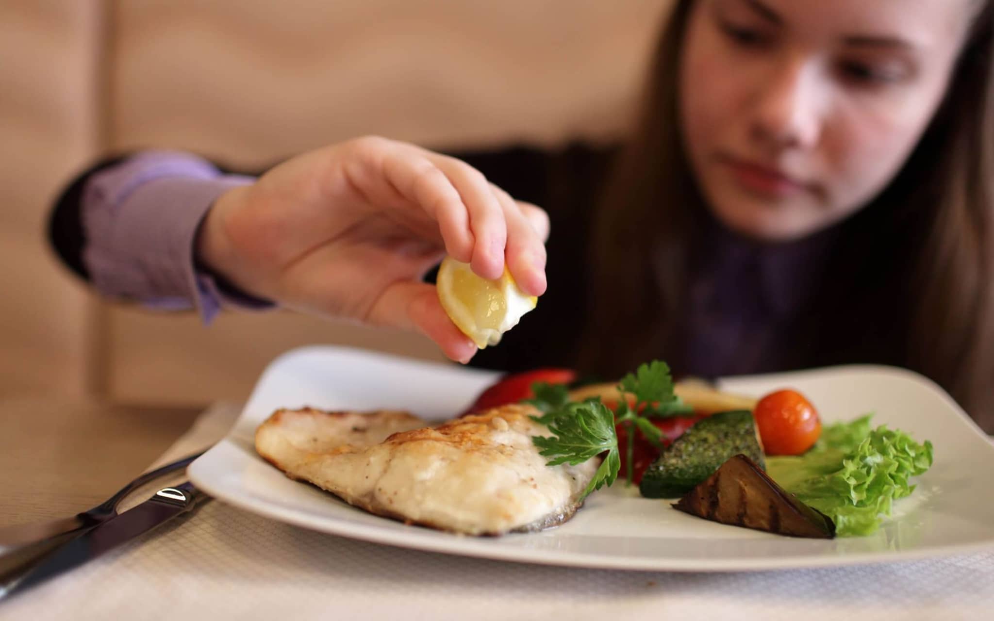 Junges Mädchen macht Zitrone auf ihren Fisch auf dem Teller