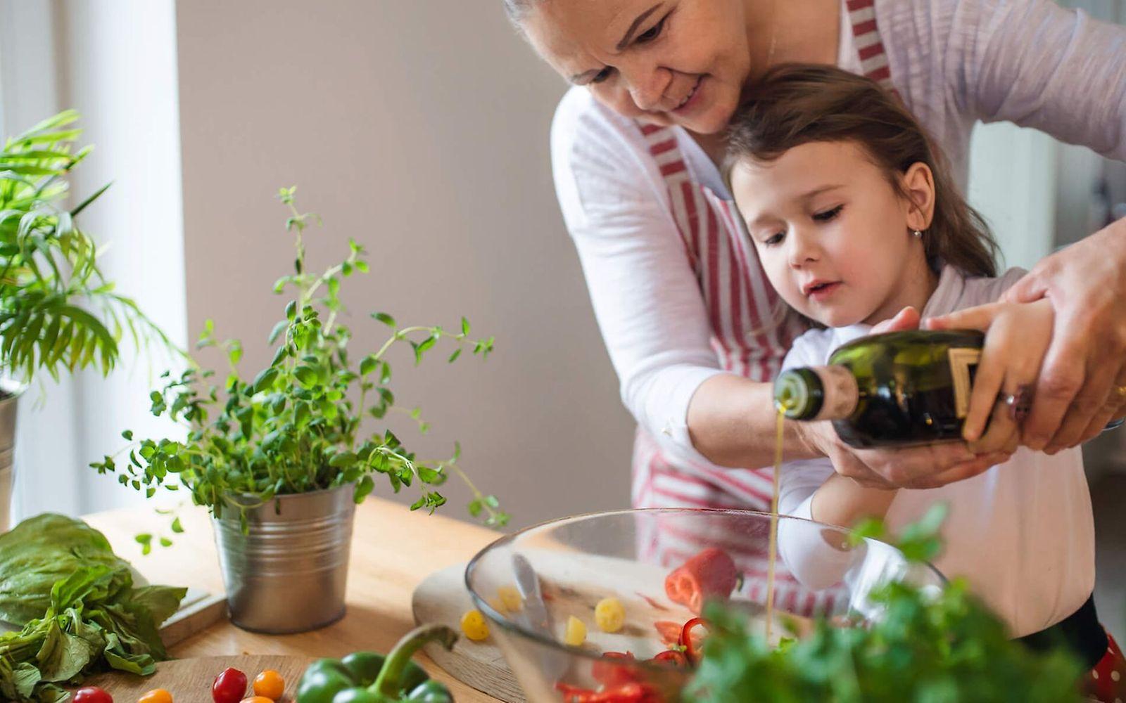 Makronährstoff Fett: Kleines Mädchen gießt gemeinsam mit seiner Mutter Öl über einen Salat.