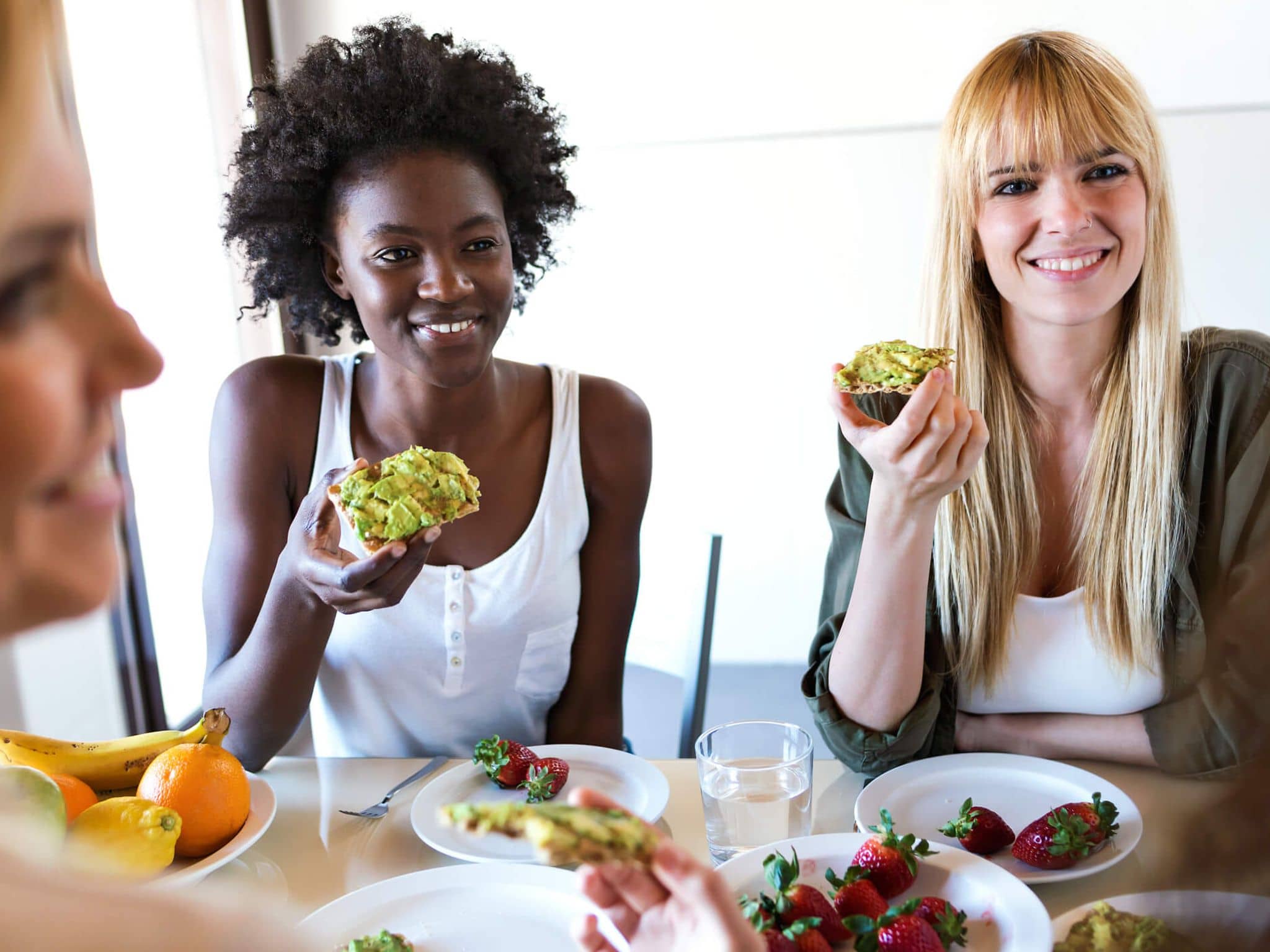 Drei junge Frauen, lachen und essen Brot mit Avocado zum Frühstück