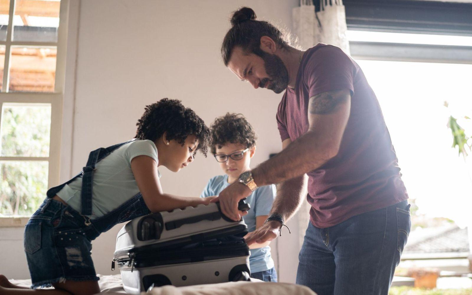 Vorbereitung Urlaub: Ein Vater packt mit zwei Kindern einen Koffer.